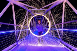 Boy playing with a sparkler type of firework on contemporary bridge, white and lilac glow