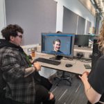 Two students looking at computer screen showing digital version of a male character