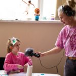 Young girl speaking into a microphone held by a woman wearing headphones